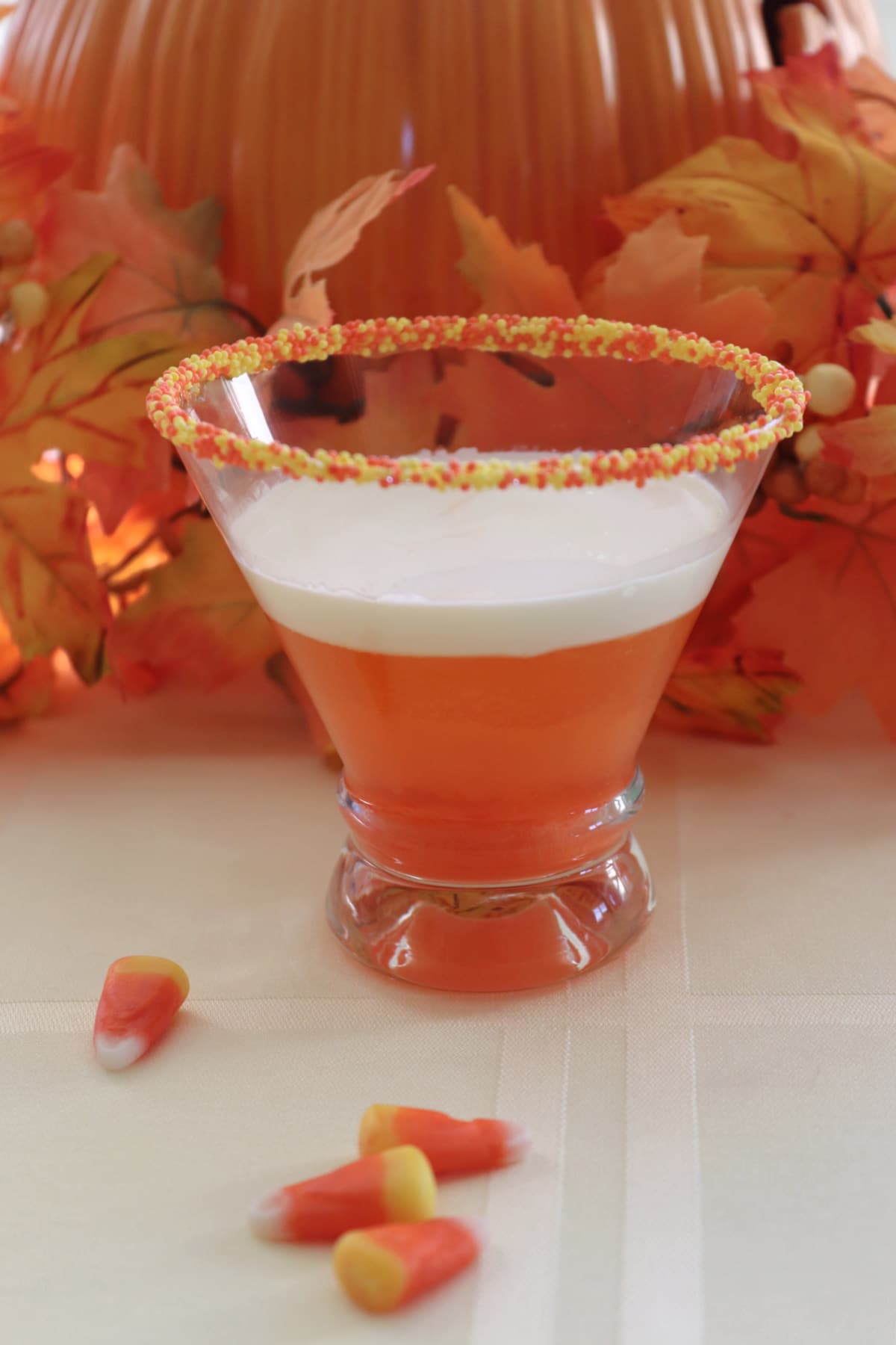 A candy corn martini on a yellow table cloth with candy around it.