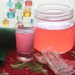 Homemade peppermint vodka in a jar and shot glass with two mini candy canes on a placemat.