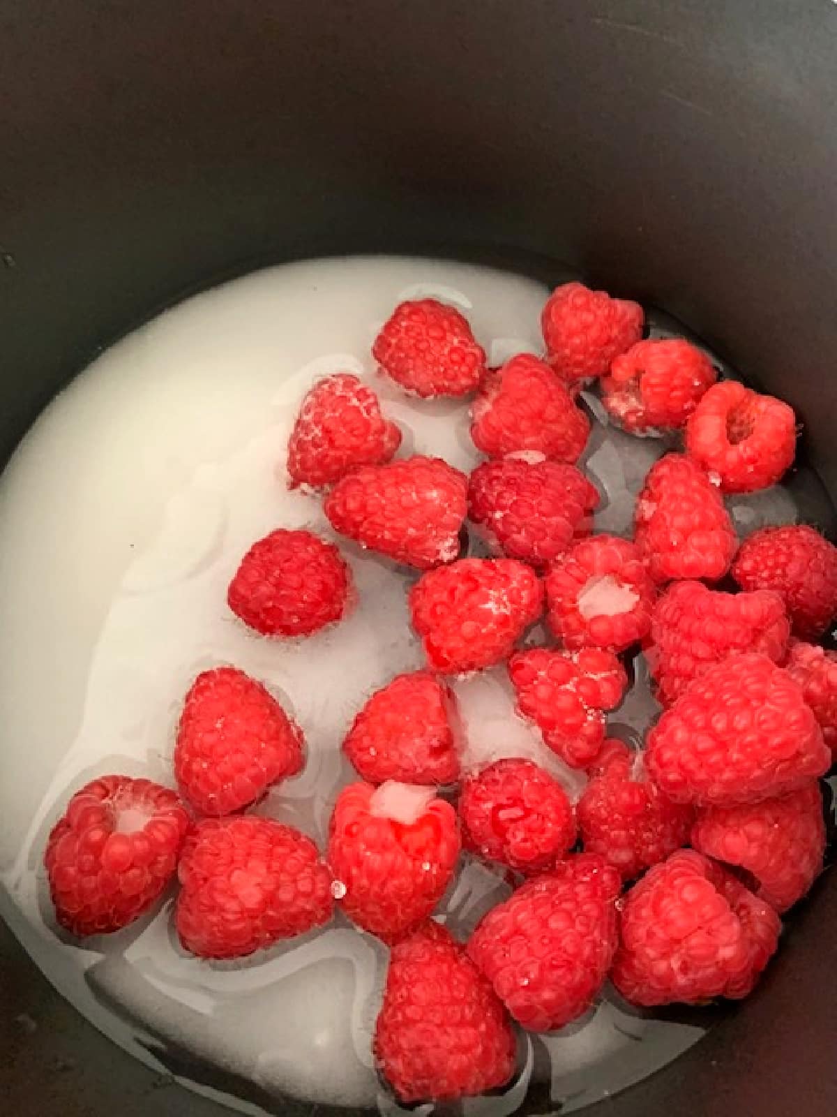 Overhead view of raspberries, sugar and water in a saucepan.