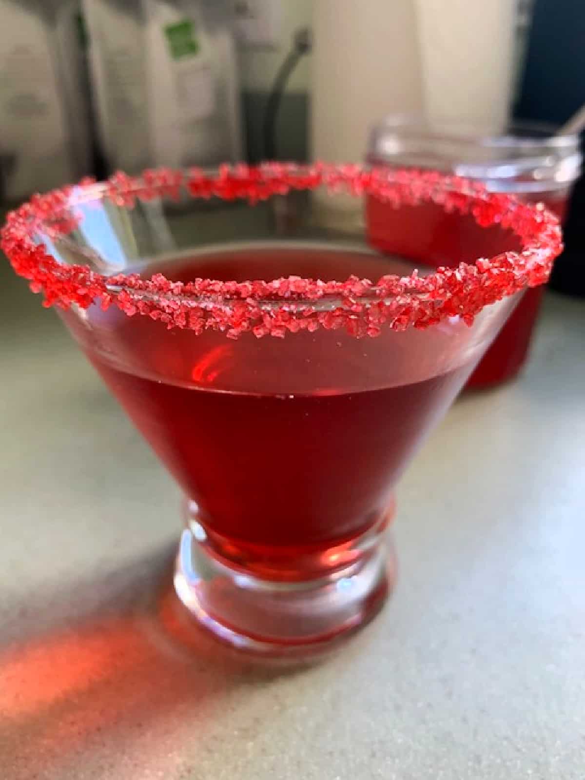 Raspberry simple syrup recipe in a clear glass with red sugar on the rim.
