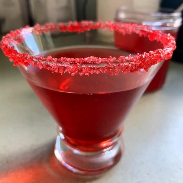 Raspberry simple syrup in a glass with red sugar on the rim for presentation.