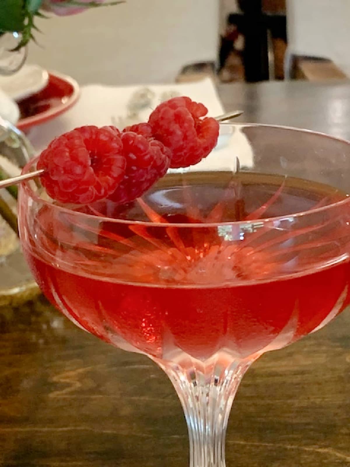 Side view of a raspberry martini in a coupe glass garnished with fresh raspberries.