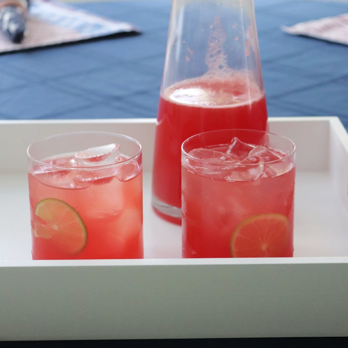 A pitcher and two glasses of watermelon agua fresca on a white tray.
