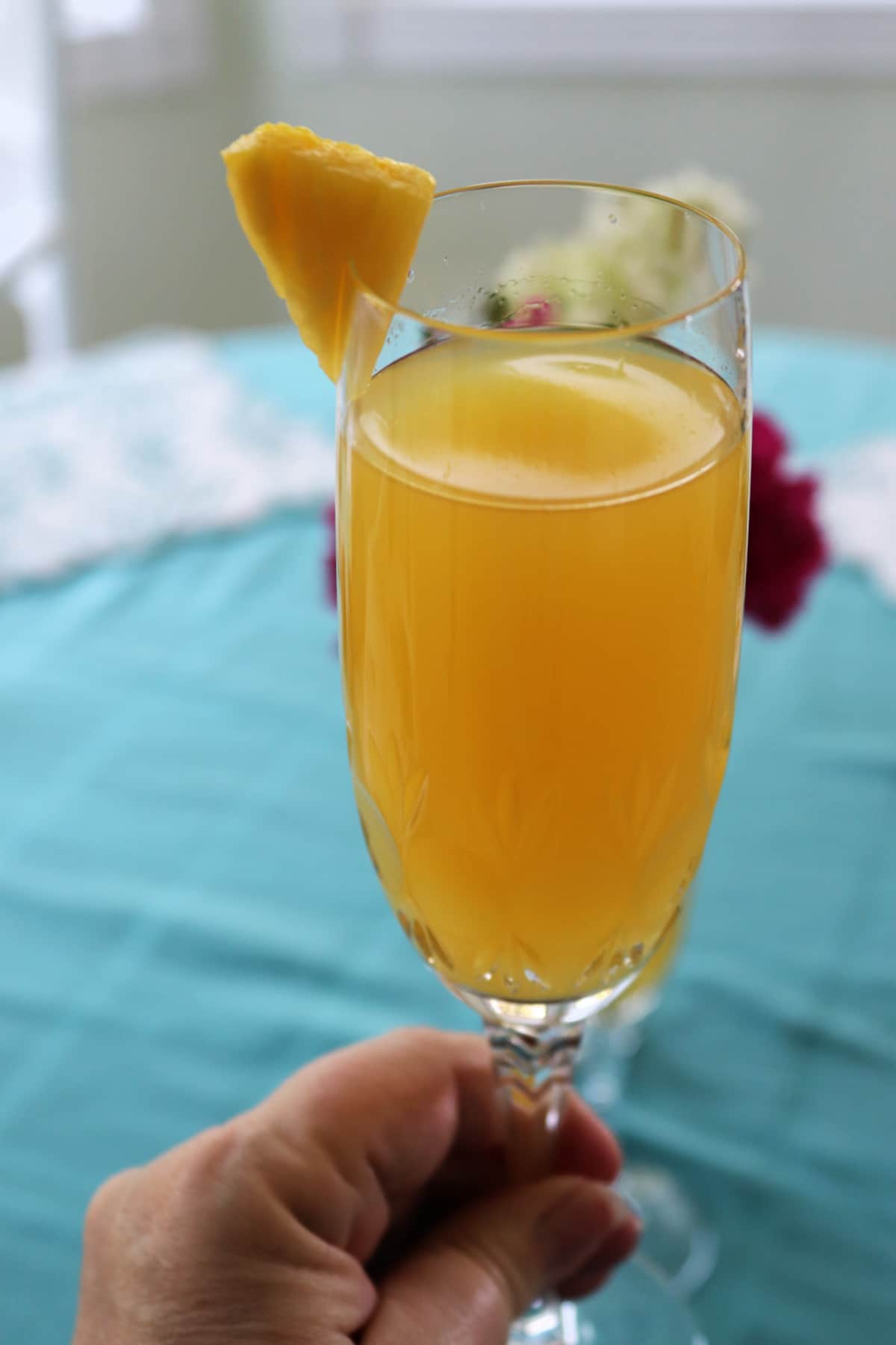 A champagne glass being held with a pineapple wedge on the rim as a garnish.