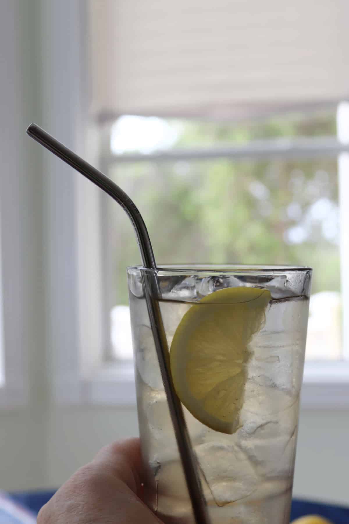 A glass of lemonade tequila with a lemon slice and straw being held.